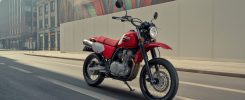 Vue de côté de la Suzuki DRZ-4SM 2025 supermotard rouge et noire sur route urbaine avec détails technologiques et la Bimota Tesi H2 Tera 2025 motorbike électrique luxe en carbone noir brillant avec cadre aluminium massif sur fond neutre studio