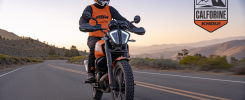 KTM 390 Adventure R moto tout-terrain orange sur route sinueuse avec pilote équipé en tenue moto technique, logo California Superbike School au-dessus.
