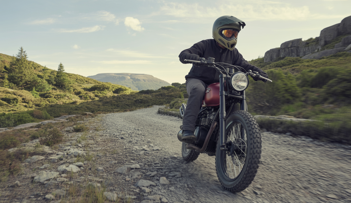 Motard expérimentant la conduite sur un chemin boueux et rocailleux dans les paysages sauvages du nord du Pays de Galles, avec montagnes et forêts en arrière-plan